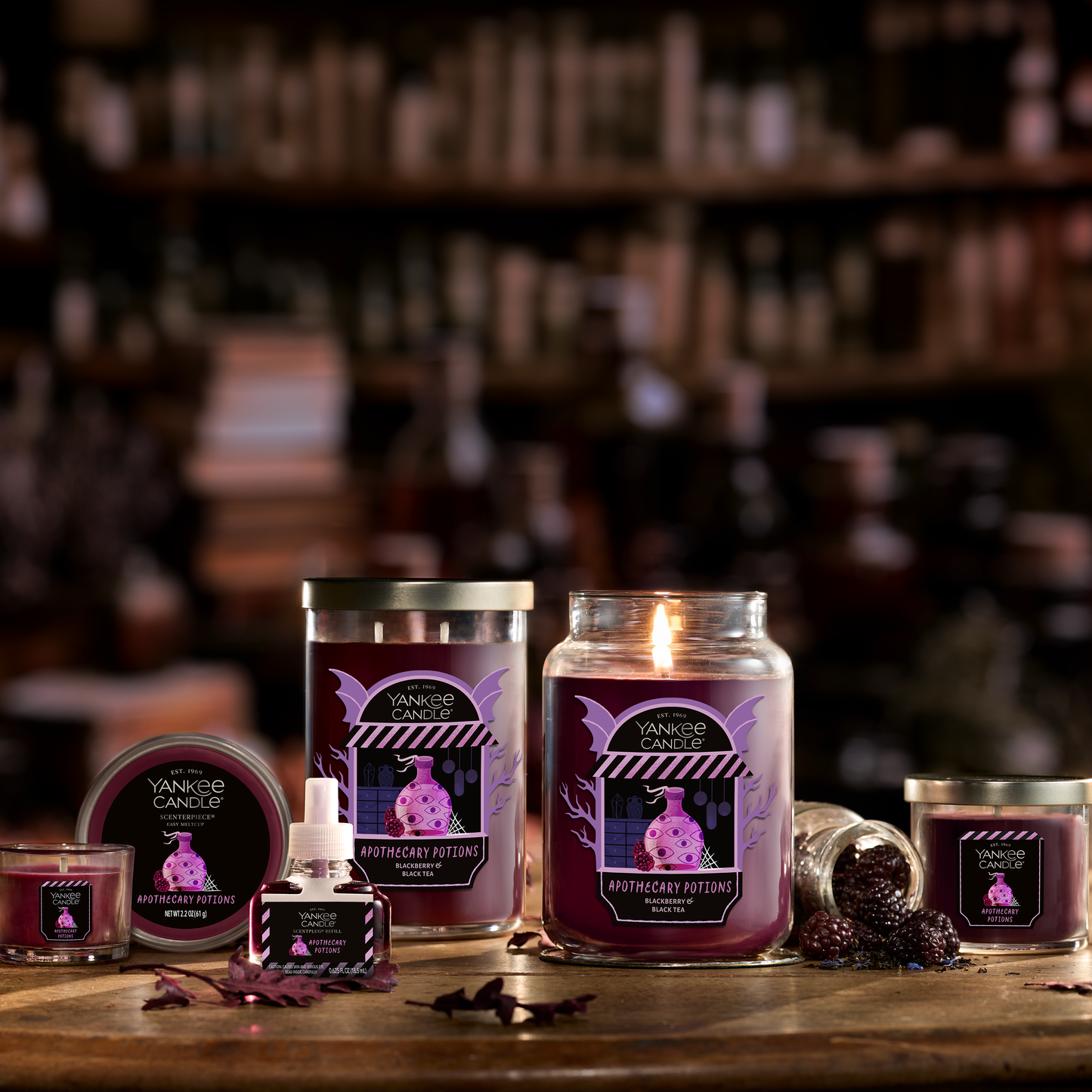 Large purple scented candle in glass jar with berries, surrounded by matching home fragrance products on a wooden table
