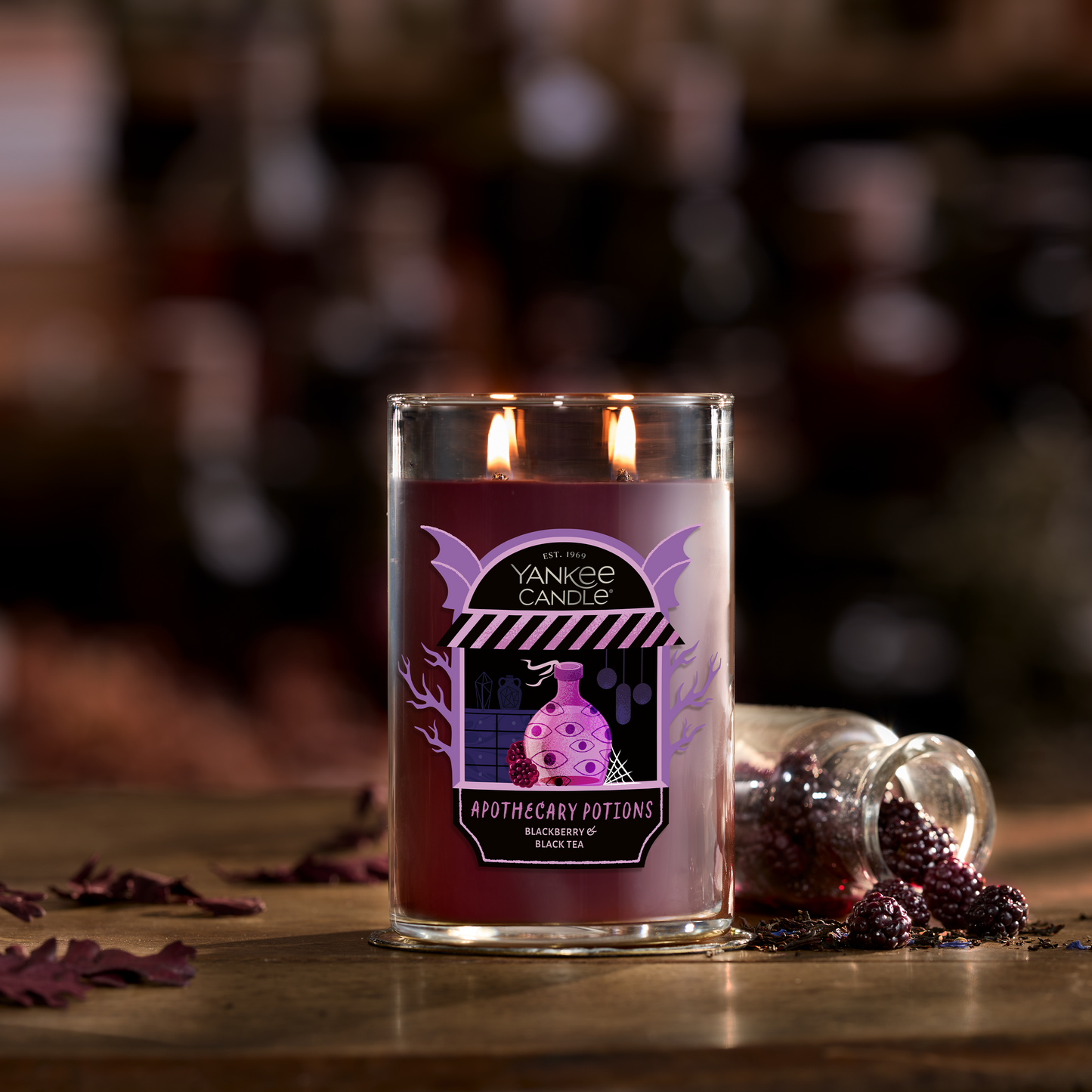 Large purple jar candle with two wicks on a rustic table, next to blackberries and a small glass jar.